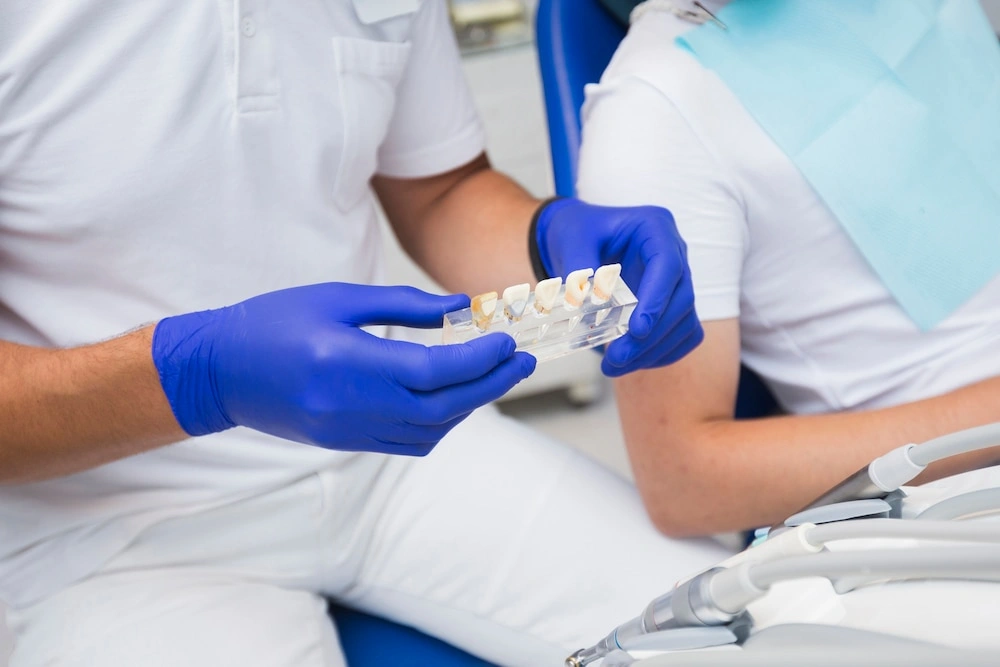 A dentist holding a dental model showing various tooth shades for a custom dental implant crown comparison with a patient.